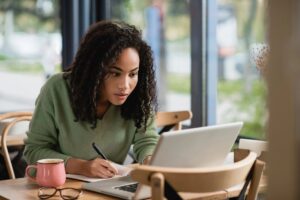 Female business owner taking notes in notepad while working on laptop for SEO and AI content creation